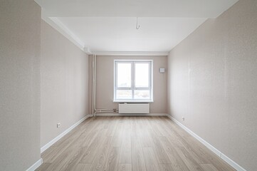 Empty room with beige walls, light wood floor, and a window. The room is bright and appears newly...