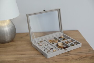 Jewelry box with many different accessories and lamp on wooden table near white wall indoors,...