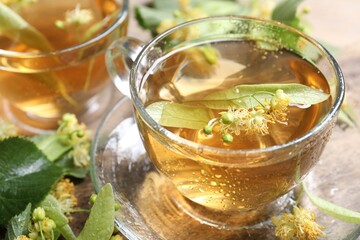 Tasty linden tea in cups, leaves and flowers on table, closeup