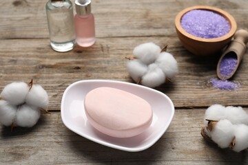 Soap bar, cosmetic products and cotton flowers on wooden table, above view