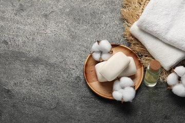 Soap bars, cosmetic product, cotton flowers and towels on grey table, flat lay. Space for text