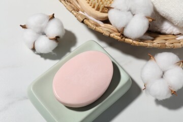 Soap bar, cotton flowers, towel and brush on white marble table, flat lay