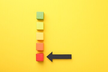 Maximum. Colorful cubes and arrow pointing at red one on yellow background, flat lay
