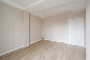 bright, empty room with light wood flooring and beige walls. A white door stands against a beige...