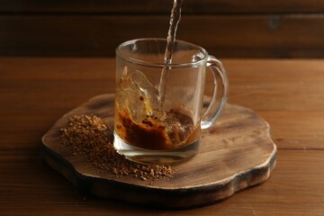 Pouring hot water into cup with instant coffee on wooden table, closeup