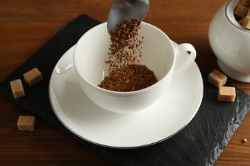 Putting granulated instant coffee into cup on wooden table, closeup