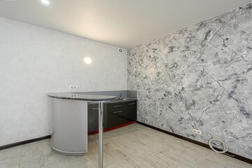 minimalist kitchen area features a small sink, a bar-style counter, and unique marbled wallpaper....