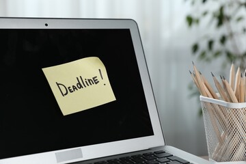Sticky note with word Deadline attached to laptop indoors