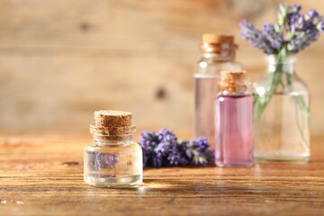 Bottles of lavender essential oil and flowers on wooden table, closeup