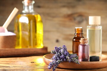 Bottles of lavender essential oil and flowers on wooden table, closeup. Space for text