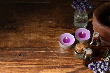 Bottles of lavender essential oil, burning candles and flowers on wooden table, above view. Space...
