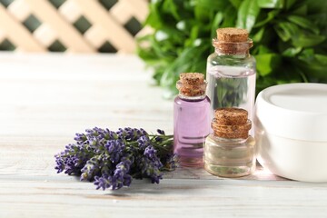 Bottles of essential oil, flowers and cream on white wooden table, closeup