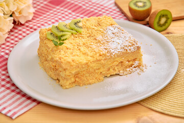 Delicious kiwi-topped napoleon cake on white plate with checkered napkin