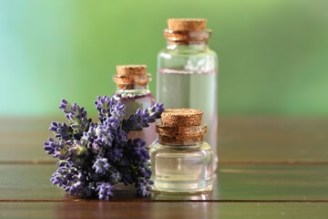 Bottles of lavender essential oil and flowers on wooden table, closeup