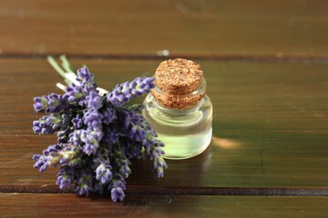 Bottle of lavender essential oil and flowers on wooden table, closeup
