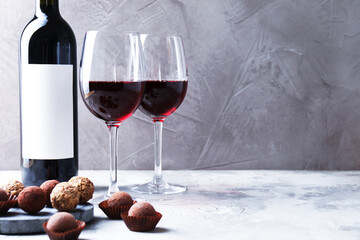 Delicious truffle bonbons and red wine on light grey background. Space for text