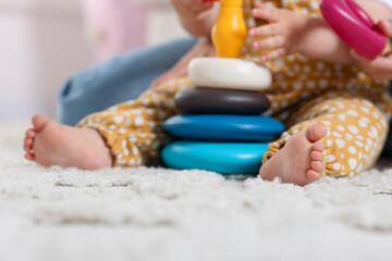 Mother and her little baby playing with toy pyramid on floor at home, closeup