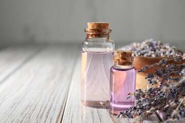 Natural essential oil and lavender flowers on white wooden table, closeup. Space for text