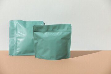 Zipper stand-up pouches on beige table against light grey background, mockup for design