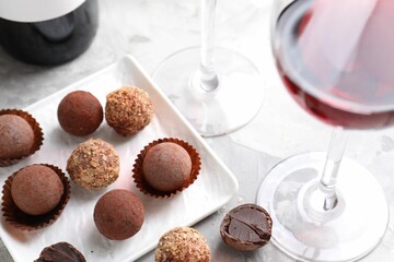 Red wine in glass and truffle bonbons on light table, closeup