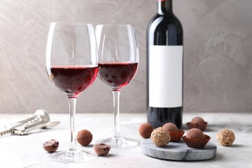 Red wine and truffle bonbons on white table against grey background, closeup