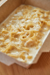 Creamy fettuccine alfredo in cardboard container on wooden table