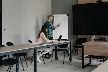 Two coworkers analyze diagrams during a meeting with supportive technology in the workplace.