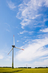 Wind turbine standing tall in a vibrant green field under a bright blue sky with fluffy clouds,...