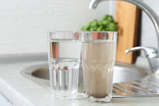 Glasses with clean and dirty water near sink indoors