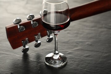 Acoustic guitar and glass of red wine on black table, closeup
