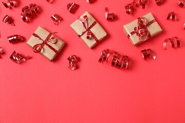Shiny serpentine streamers and gift boxes on red background, flat lay. Space for text