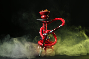 Hookah on wooden table with smoke against black background