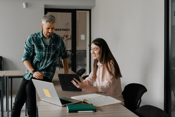 Two professionals collaborating in an office, using devices to discuss and share ideas.