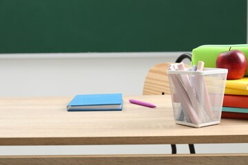 Different school stationery and red apple on wooden table near blackboard indoors