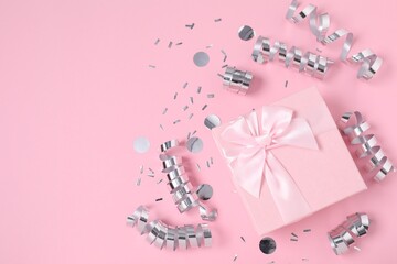 Shiny party streamers, confetti and gift on pink background, flat lay. Space for text
