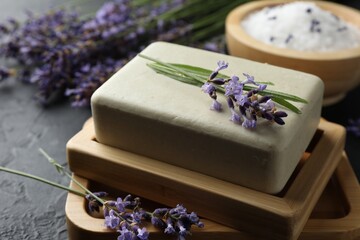 Aromatic soap bar and lavender flowers on dark textured table, closeup