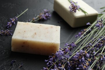 Aromatic soap bars and lavender flowers on dark textured table, closeup