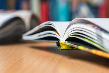 Open hardcover book lying on a light wooden desk with a blurred pastel background, close-up view