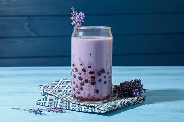 Tasty milk bubble tea in glass and lavender flowers on light blue wooden table, closeup