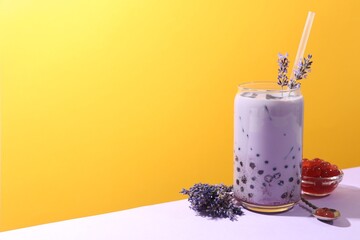 Tasty milk bubble tea in glass and lavender flowers on white table against orange background, space...