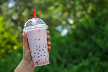 Woman with tasty milk bubble tea in plastic cup outdoors, closeup. Space for text