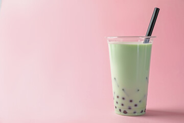Tasty milk bubble tea in plastic cup on pink background. Space for text