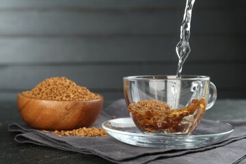Pouring hot water into cup with instant coffee at black table, closeup