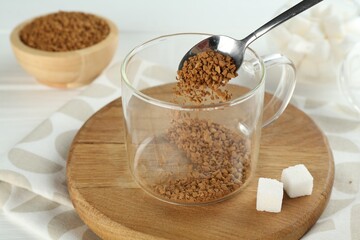 Putting instant coffee into cup at light table, closeup