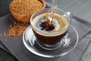 Pouring hot water into cup with instant coffee at black table, closeup