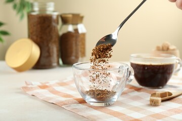 Woman putting instant coffee into cup at light table, closeup