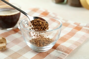 Putting instant coffee into cup at light table, closeup
