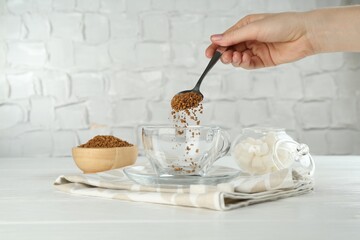 Woman putting instant coffee into cup at light table, closeup