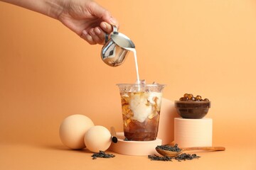 Woman pouring milk into bubble tea on orange background, closeup