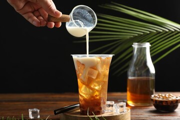 Woman pouring milk into bubble tea at wooden table, closeup